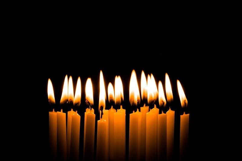 '火がついた複数の和ろうそくが黒い背景に並ぶ'