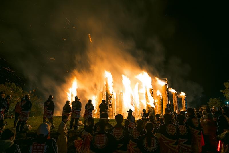 燃え上がる松明あかしを取り囲む観客たち、夜空に立ち上る炎と白煙