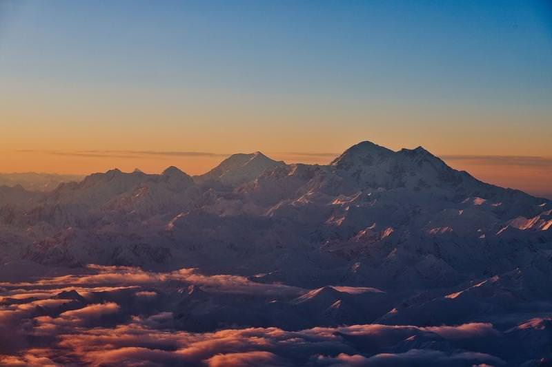 'オレンジ色に染まる夕暮れのデナリの雪山と雲海'