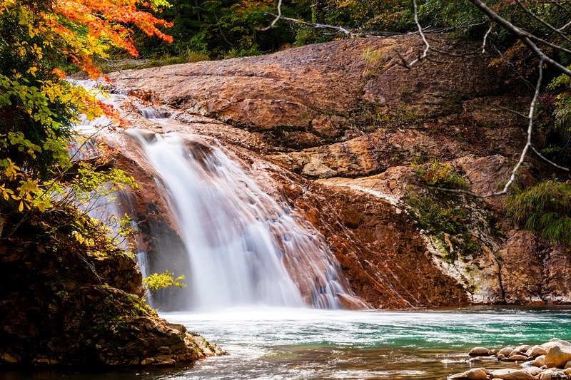 '秋の渓谷に流れる赤滝と紅葉の風景'