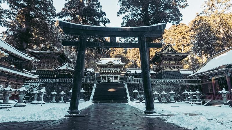 雪が積もった大きな黒い鳥居と奥の本殿が見える日光東照宮