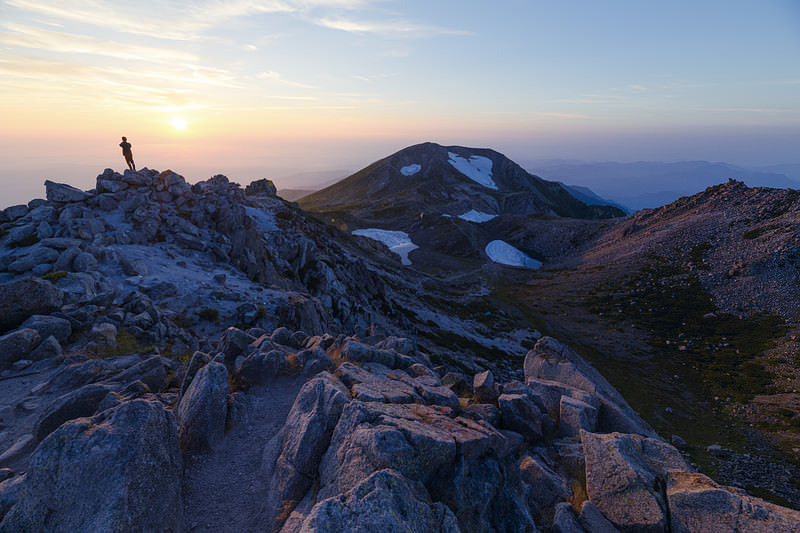 '日本海に沈む夕日を眺める白山御前峰の登山者'