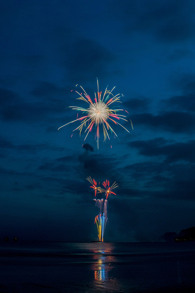 '花火大会を砂浜から撮影した夜空と海上花火'