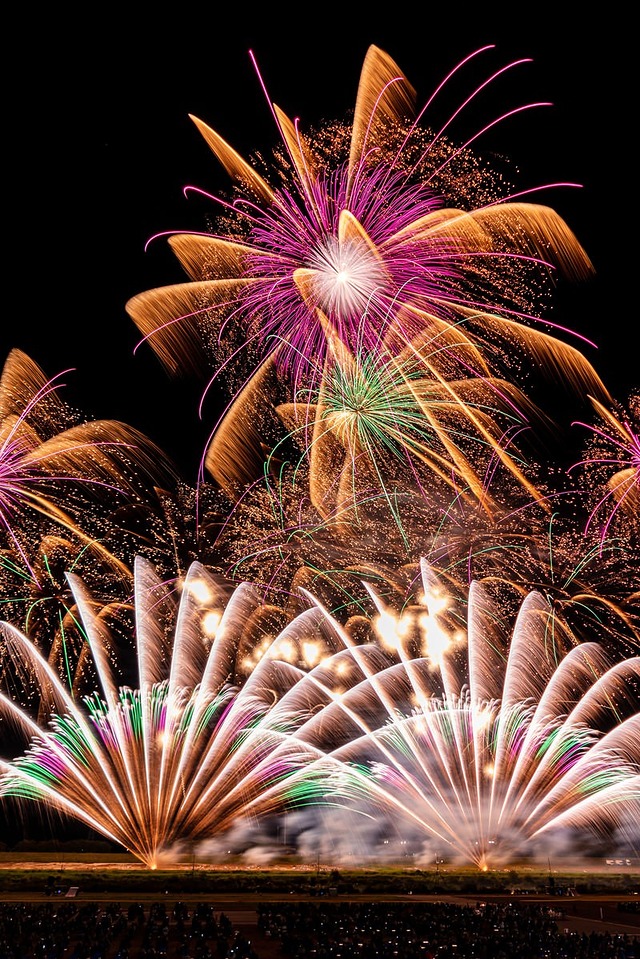 '一斉にはじける打上げ花火、色とりどりのスパークが夜空に光跡を描く'